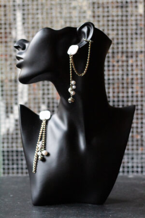 schwarzer Büstenkopf mit Ohrring. Weißer Stecker, Metallketten, unten Perlen aus Kunststoff. Ein Ohrring mit Earcuff