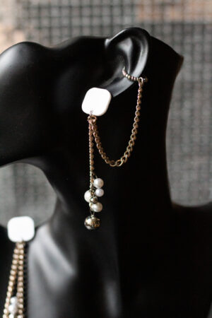 schwarzer Büstenkopf mit Ohrring. Weißer Stecker, Metallketten, unten Perlen aus Kunststoff. Ein Ohrring mit Earcuff