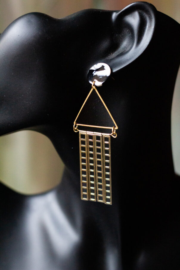 Detailaufnahme schwarze Büste mit Ohrring schwarz weißer Stecker, Messingdreieck, goldene Metallstäbe unten