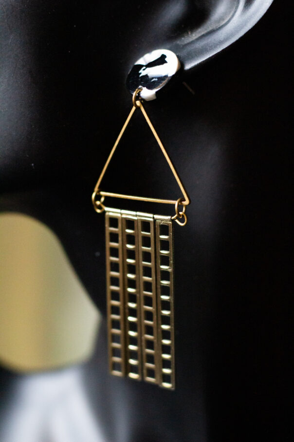 Detailaufnahme schwarze Büste mit Ohrring schwarz weißer Stecker, Messingdreieck, goldene Metallstäbe unten