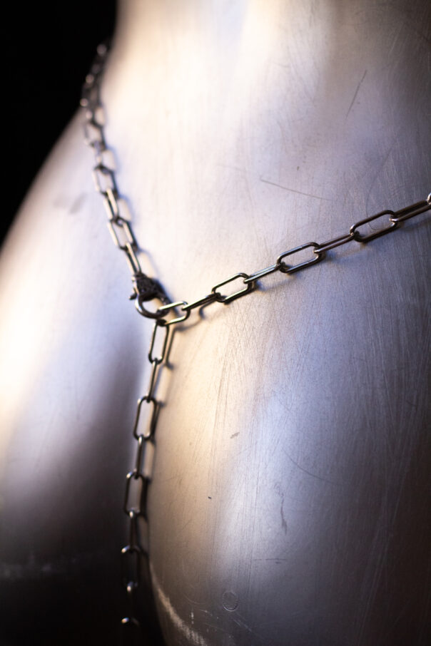 Detailaufnahme Torso mit Bodykette aus Edelstahl und buntem Anhänger in der Mitte